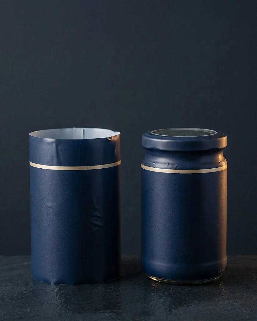 Custom shrink sleeve shown flat before shrinking next to the same sleeve shrunk tight around a jar